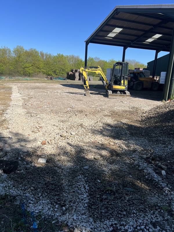 Yellow Yanmar mini digger beside a barn on stone-reinstated ground