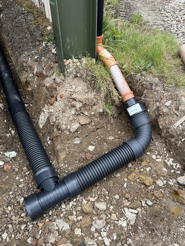 Building downpipe connected through orange pipe to black twin-wall drainage pipe with a junction