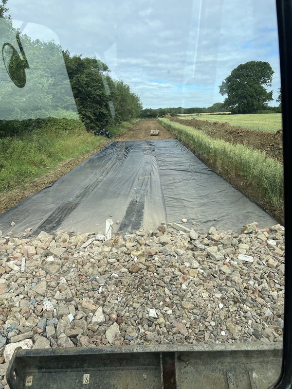 Crushed hardcore being spread over the geotextile membrane, seen from the digger cab