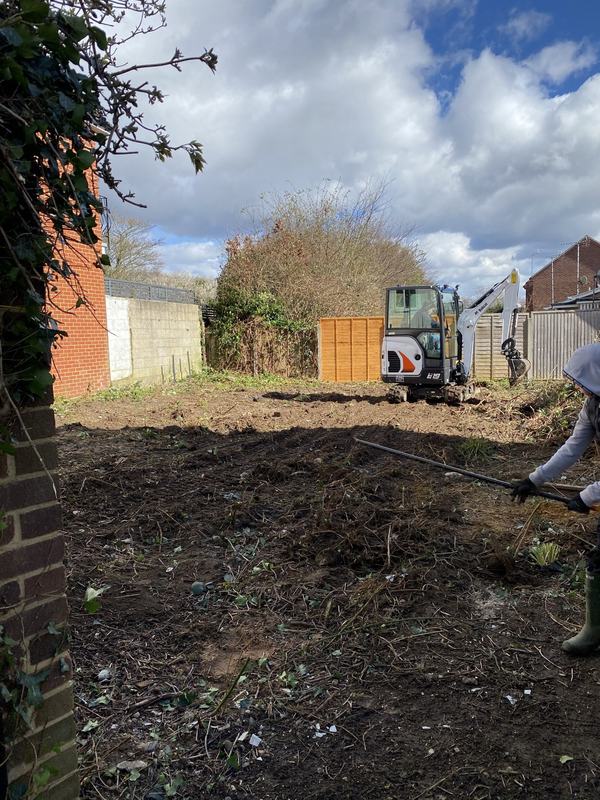 Garden plot cleared to soil with a Bobcat mini digger, and a worker raking at the edge