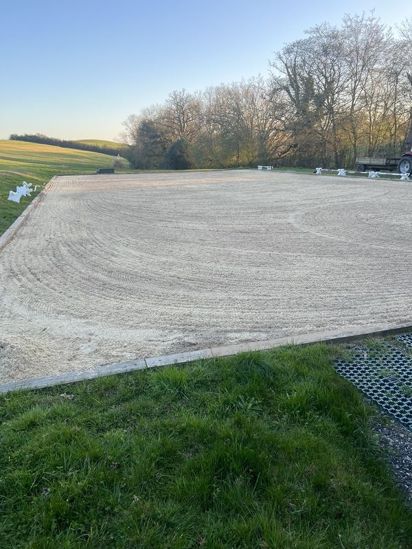 Finished ménage with a freshly harrowed, even surface in curved lines, timber edging and grass in the foreground