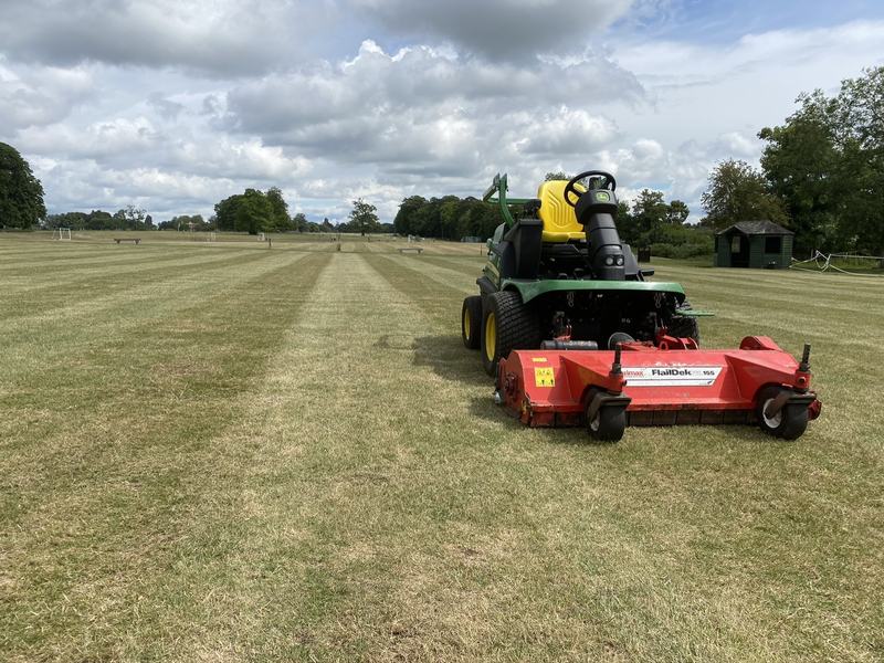 John Deere ride-on mower with a red flail deck on striped mown grass in parkland