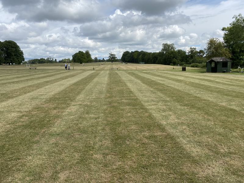 Large playing field freshly mown in neat light and dark stripes, with trees and a pavilion behind